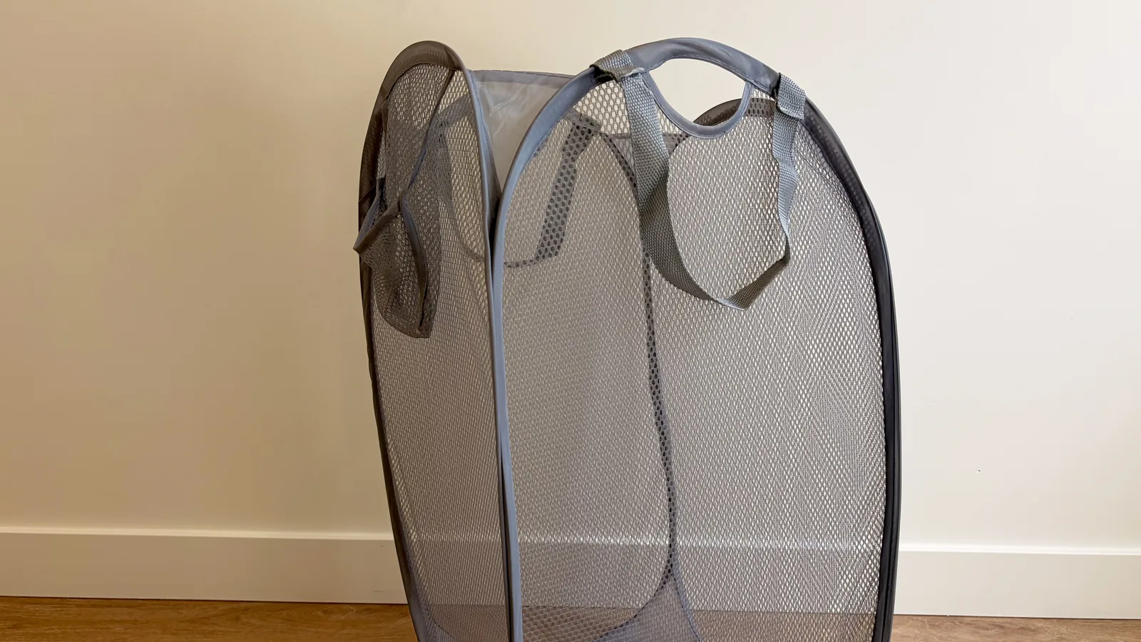 A gray mesh pop-up laundry hamper standing open on a wood floor