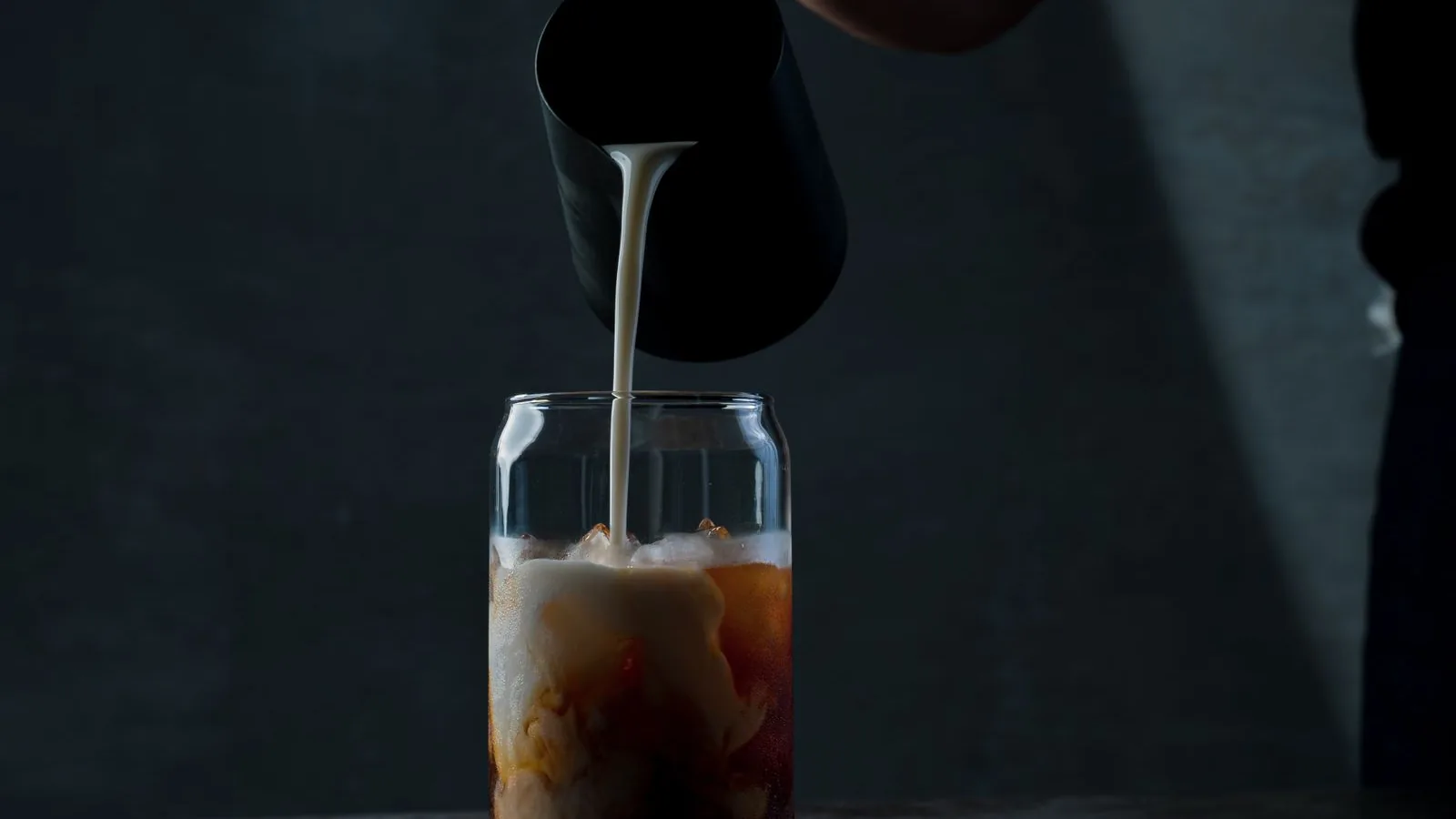 Cream pouring into a glass of iced coffee, swirling through the ice