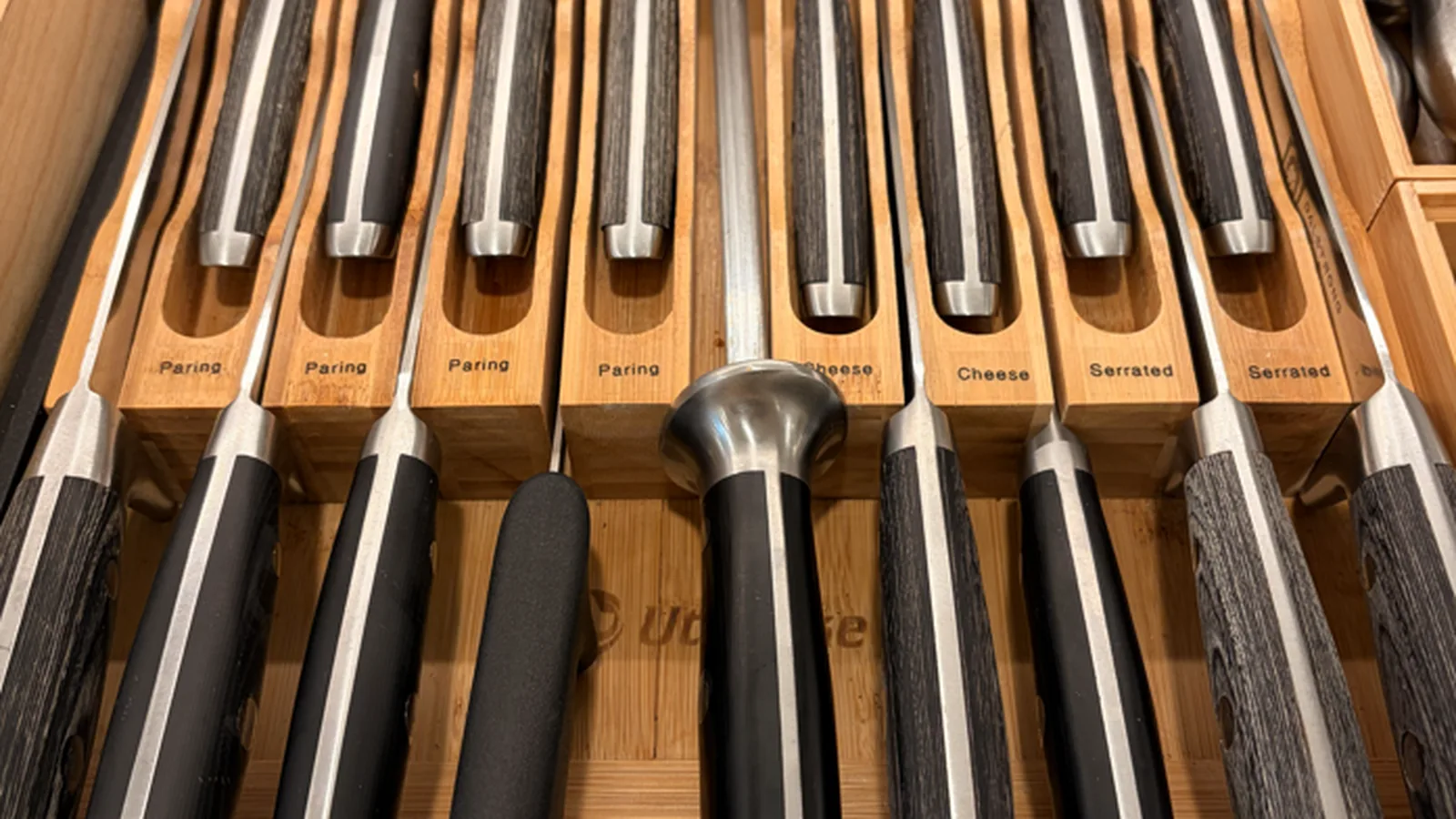 A bamboo in-drawer knife organizer with labeled slots for paring, cheese, and serrated knives